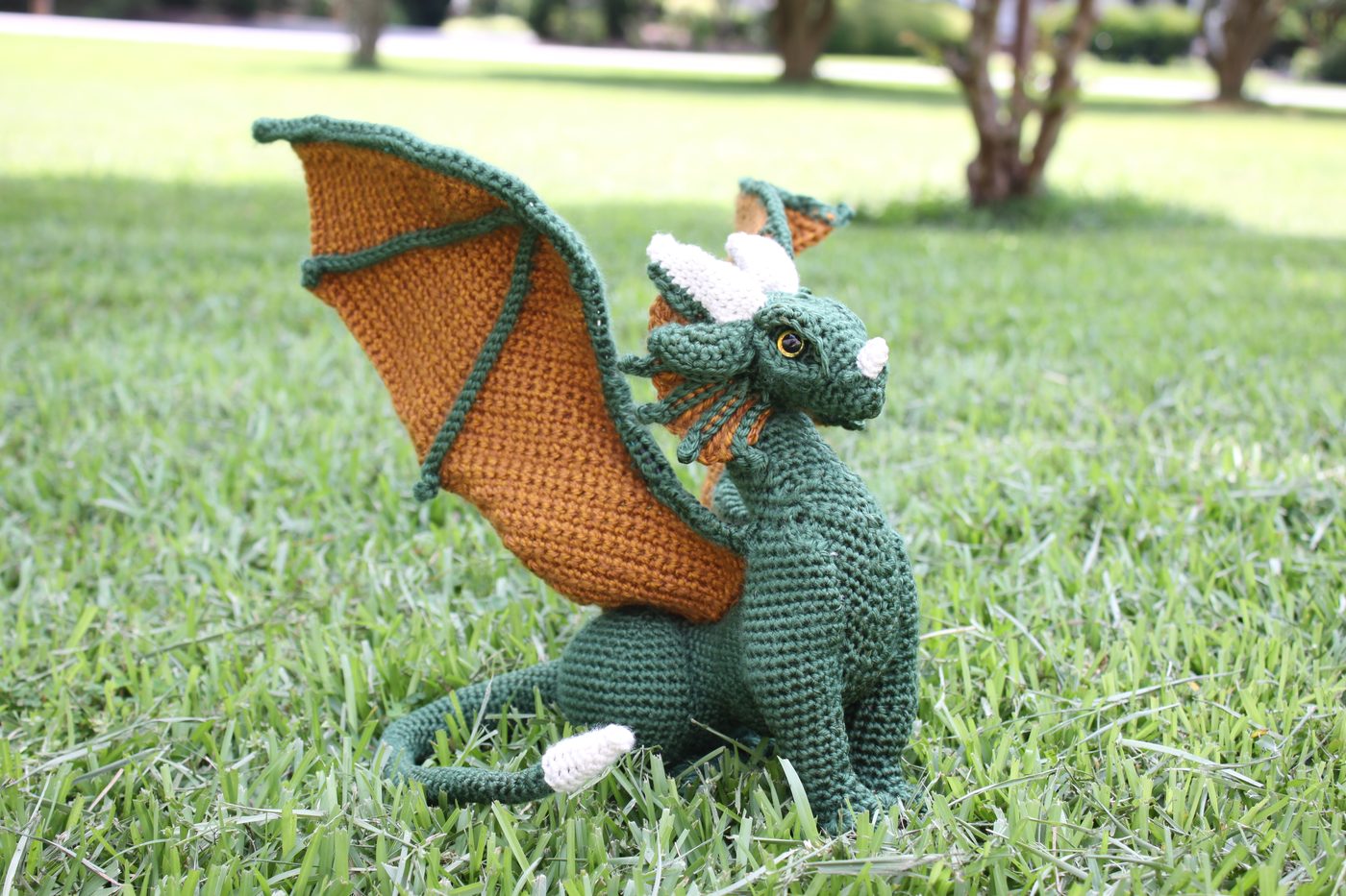 Francis, a green and gold crochet dragon, sitting in grass