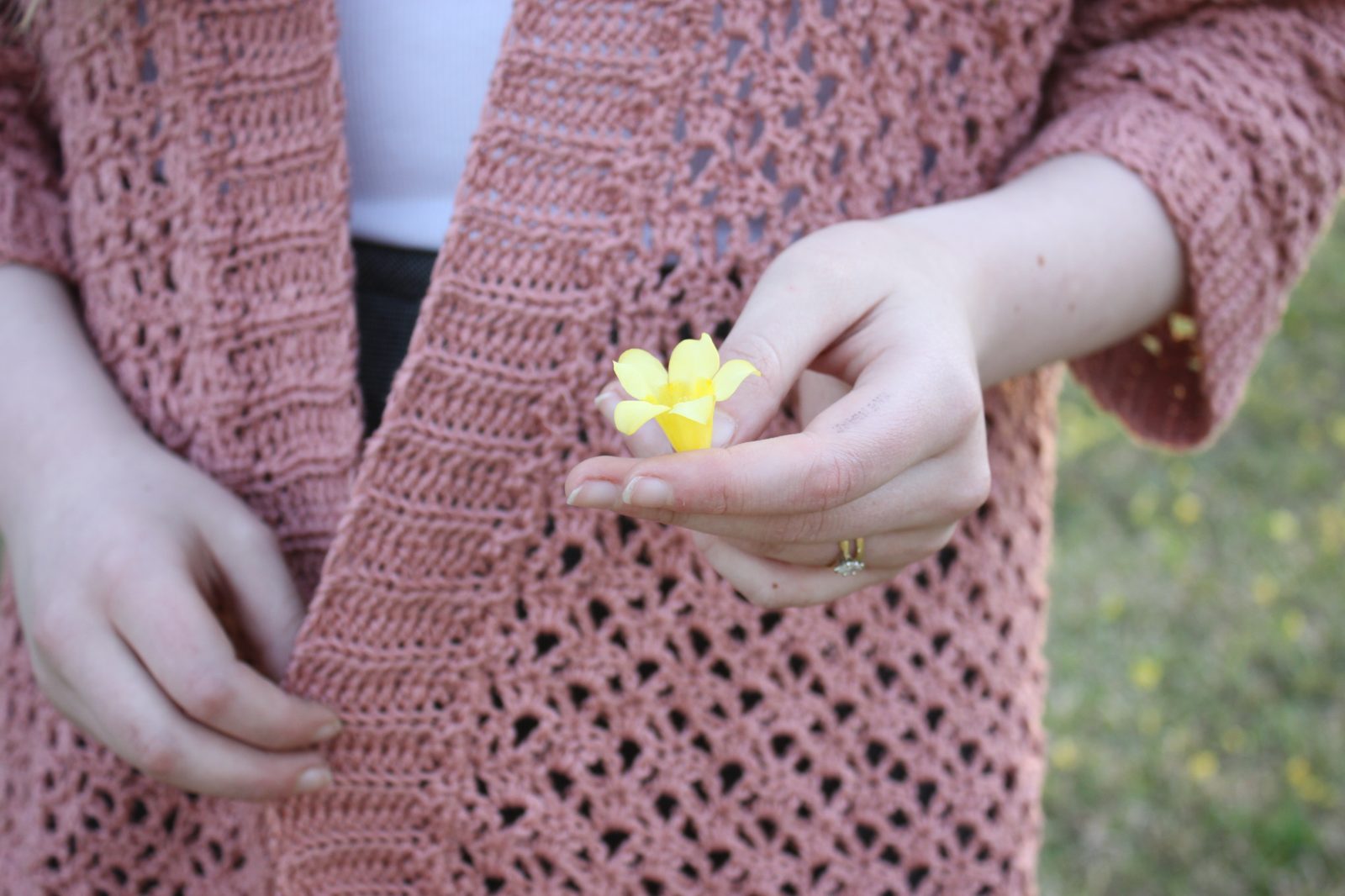 Hands in a pink crochet sweater, holding a small yellow flower