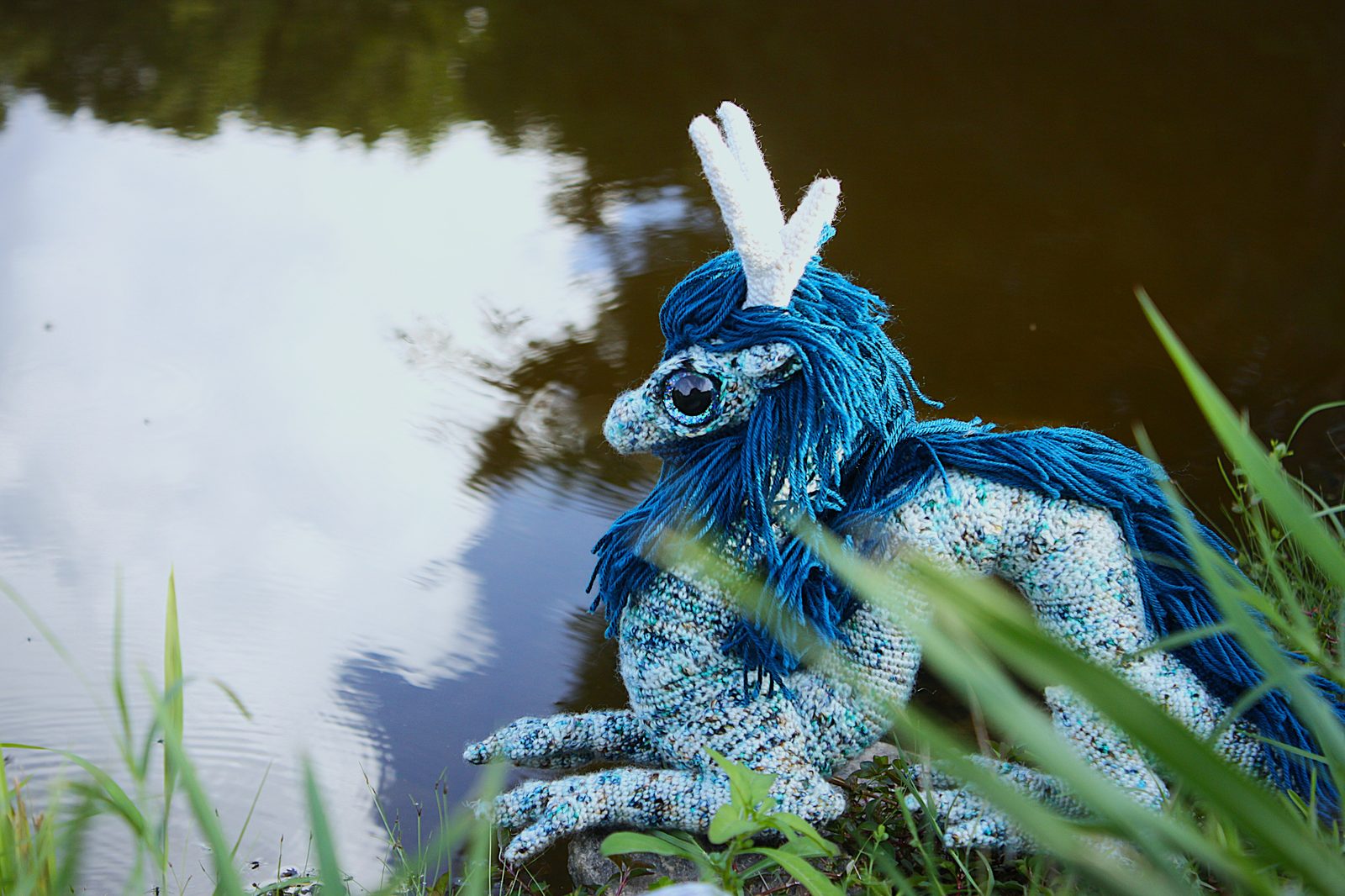 Hayase, a white and turquoise Eastern dragon, sitting waterside in grass